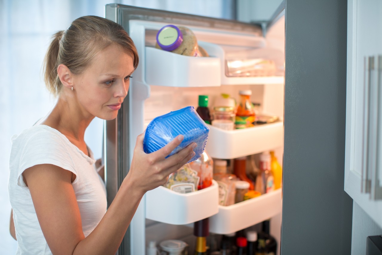Person in the kitchen next to the refrigerator looking at the expiration date of a product they have taken out of their refrigerator.