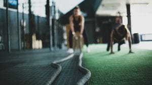 One woman doing pushups and another doing battle ropes in the gym.  Image by Meghan Holmes via Unsplash.com.